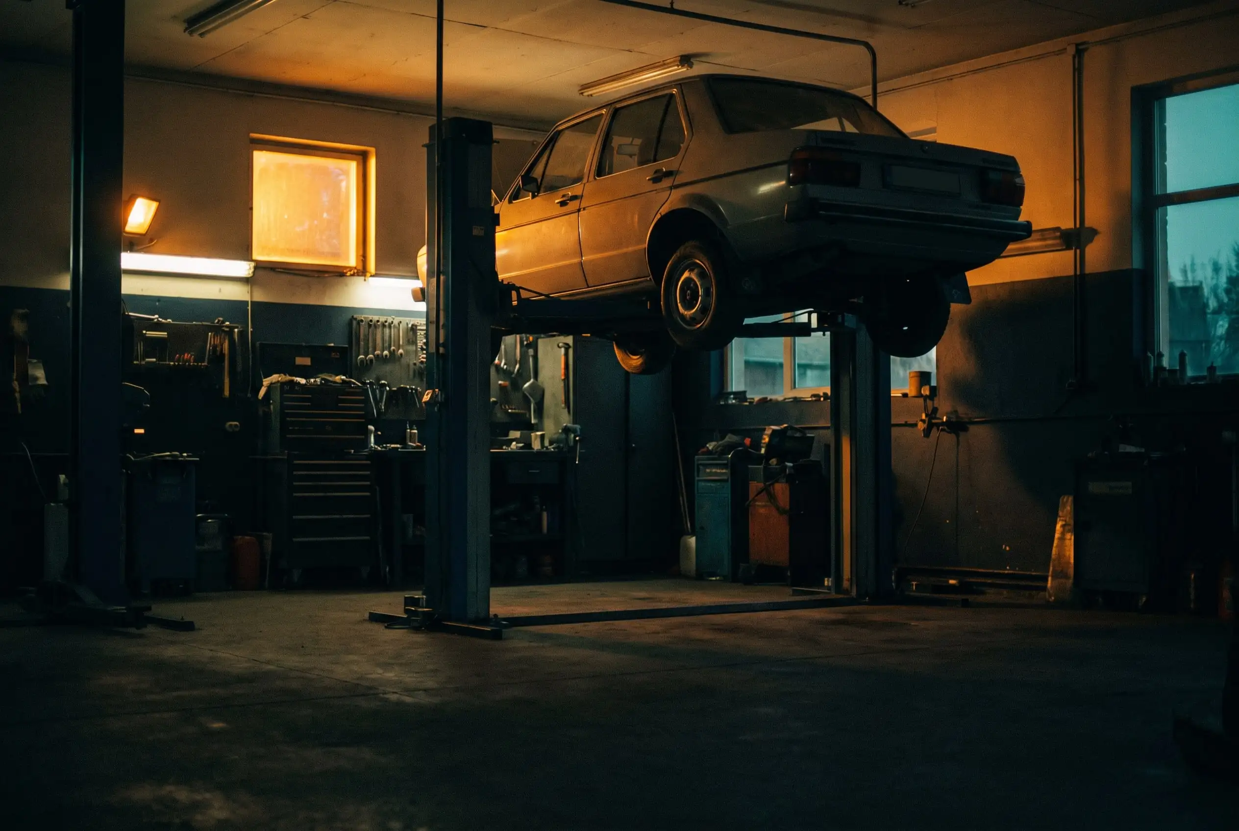 Auto uniesione wysoko na podnośniku dwukolumnowym w ciepło oświetlonym warsztacie o zmierzchu